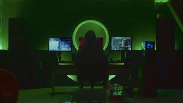 The main character sits at a desk under a green light in the Hello Stranger review, reflecting the game's tense atmosphere.