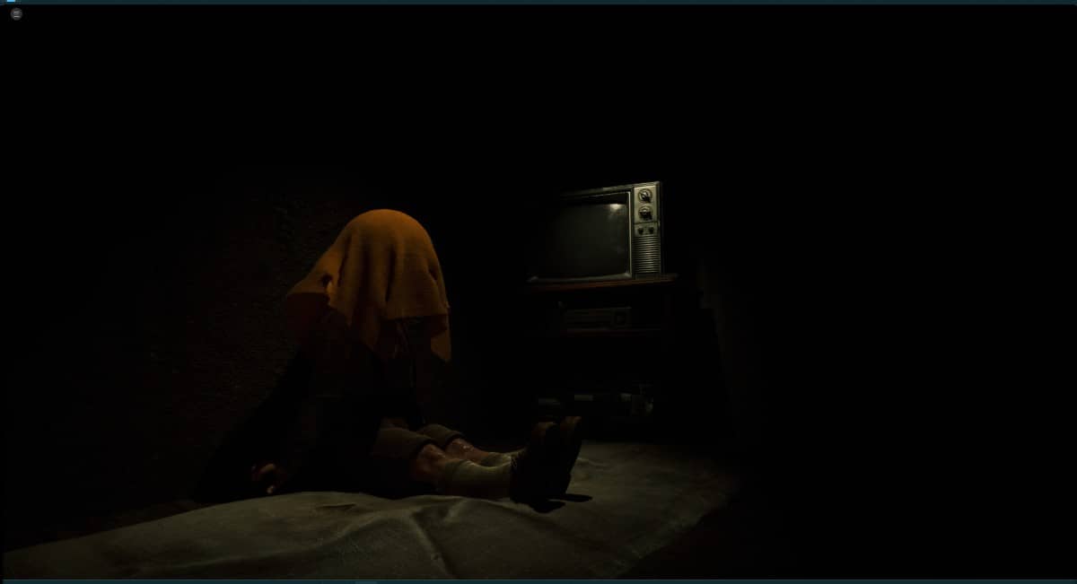 A disturbing scene in The Cabin Factory showing a teddy or boy under a towel beside a glowing TV.
